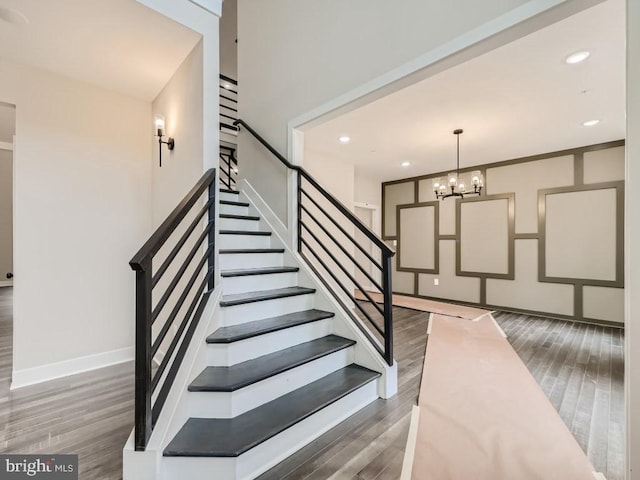 stairs featuring recessed lighting, wood finished floors, and an inviting chandelier