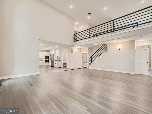 unfurnished living room with a high ceiling and light wood-type flooring