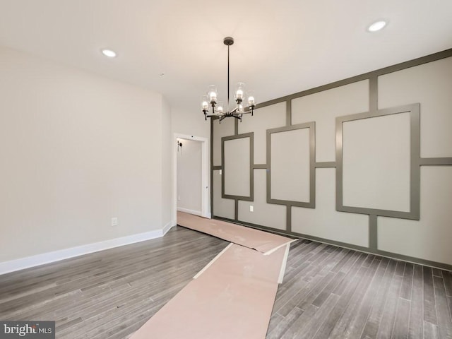 unfurnished dining area featuring baseboards, recessed lighting, wood finished floors, and an inviting chandelier