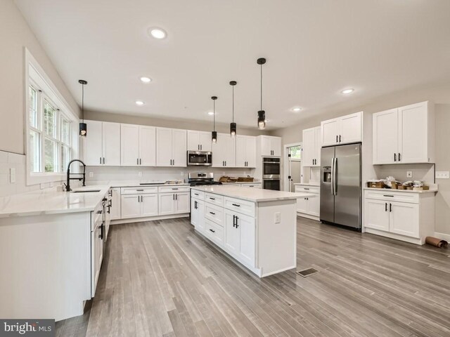 kitchen with a center island, decorative light fixtures, light hardwood / wood-style floors, white cabinetry, and stainless steel appliances