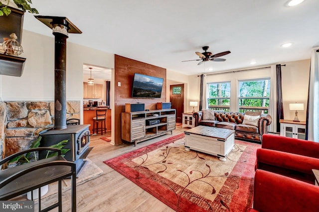 living room with light hardwood / wood-style flooring, a wood stove, and ceiling fan