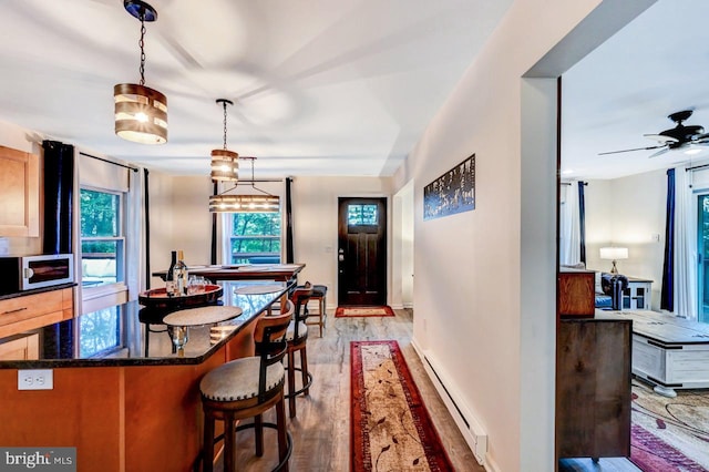 kitchen featuring pendant lighting, a kitchen breakfast bar, ceiling fan, a baseboard radiator, and wood-type flooring