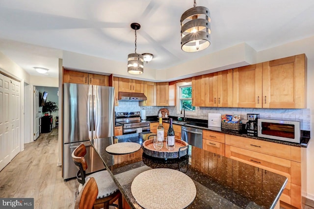 kitchen featuring appliances with stainless steel finishes, light wood-type flooring, hanging light fixtures, and dark stone counters