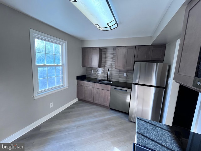 kitchen with stainless steel appliances, dark countertops, decorative backsplash, a sink, and light wood-type flooring