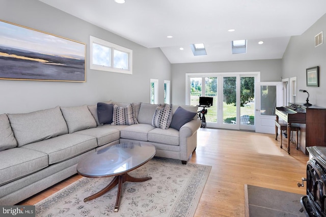 living area featuring vaulted ceiling with skylight, light wood finished floors, visible vents, and recessed lighting