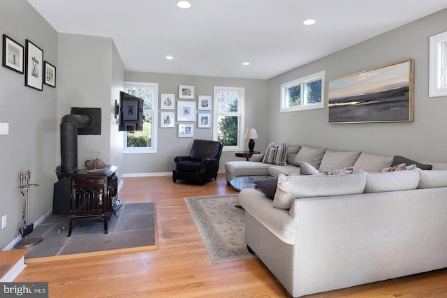 living room featuring recessed lighting, a wood stove, baseboards, and wood finished floors