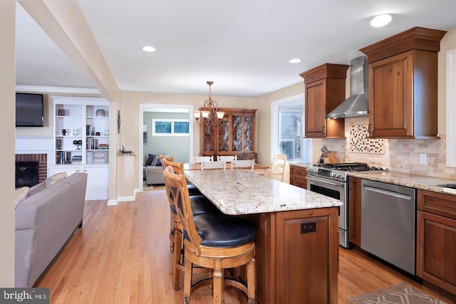 kitchen featuring wall chimney exhaust hood, open floor plan, a center island, hanging light fixtures, and stainless steel appliances