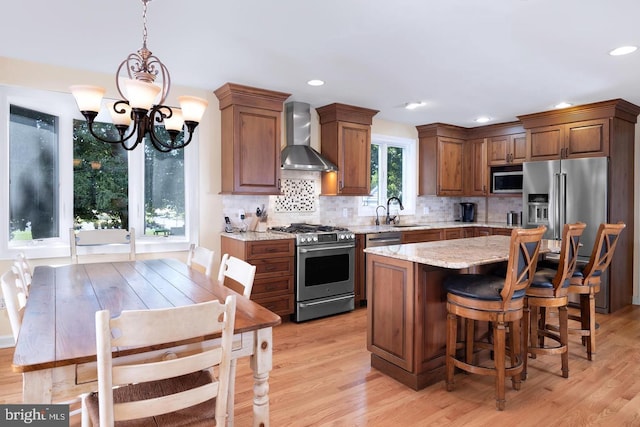 kitchen featuring light stone counters, stainless steel appliances, a kitchen island, wall chimney range hood, and decorative light fixtures