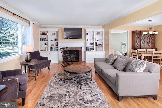 living room with ornamental molding, a fireplace, light wood-style flooring, and an inviting chandelier