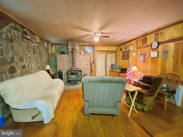 living area featuring ceiling fan, light wood finished floors, a wood stove, and wooden walls