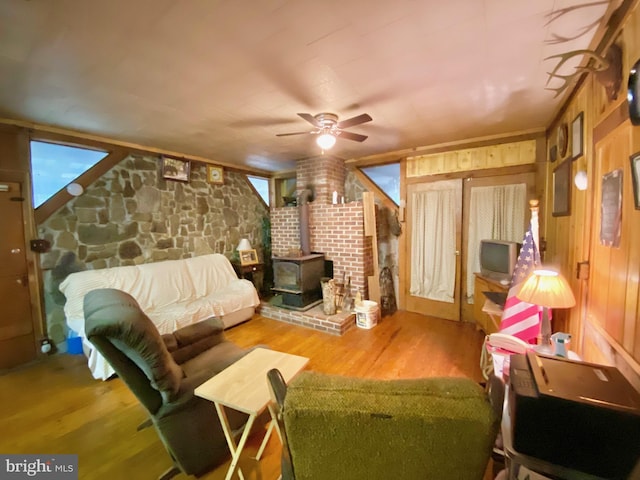 living room featuring a wood stove, wood walls, ceiling fan, and wood finished floors