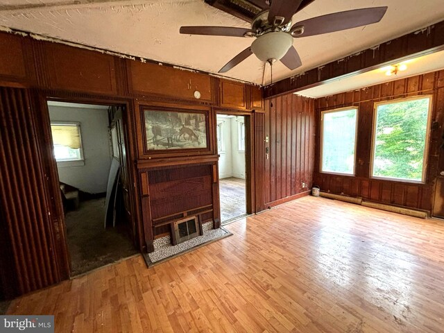 unfurnished room with ceiling fan, wood walls, light hardwood / wood-style floors, and a baseboard radiator