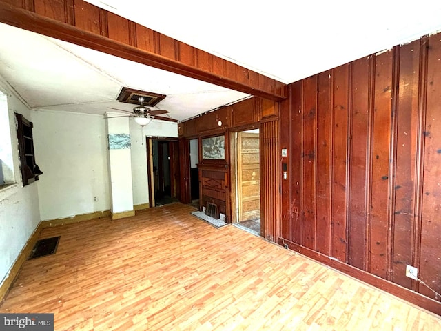 unfurnished room with visible vents, ceiling fan, wood walls, wood finished floors, and beamed ceiling