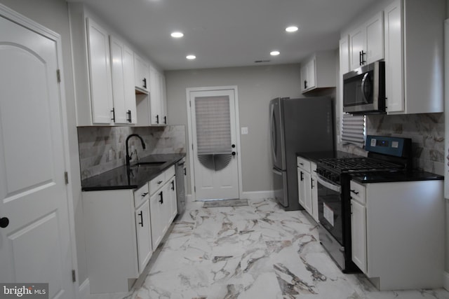 kitchen featuring marble finish floor, dark countertops, appliances with stainless steel finishes, white cabinets, and a sink