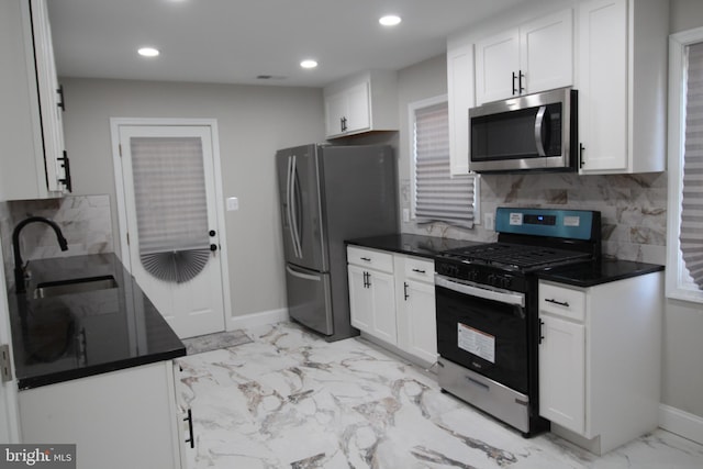 kitchen with appliances with stainless steel finishes, dark countertops, white cabinets, and a sink