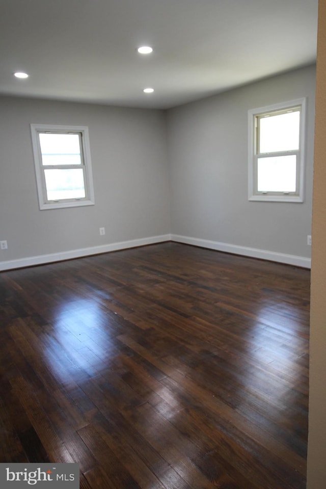 empty room with baseboards, dark wood-type flooring, and a wealth of natural light