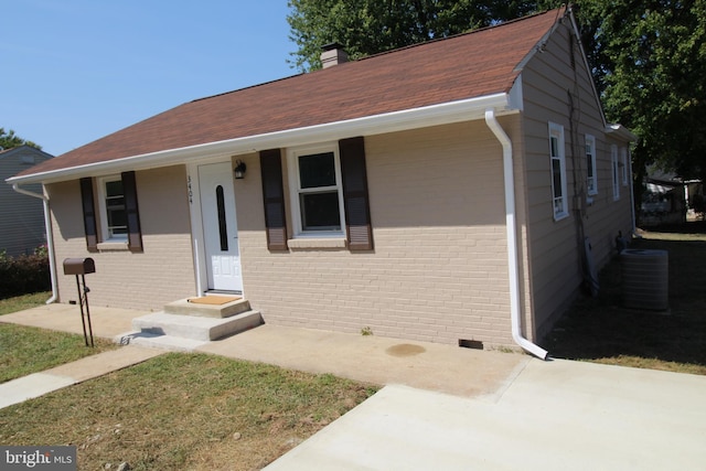 bungalow with brick siding, a chimney, and central air condition unit