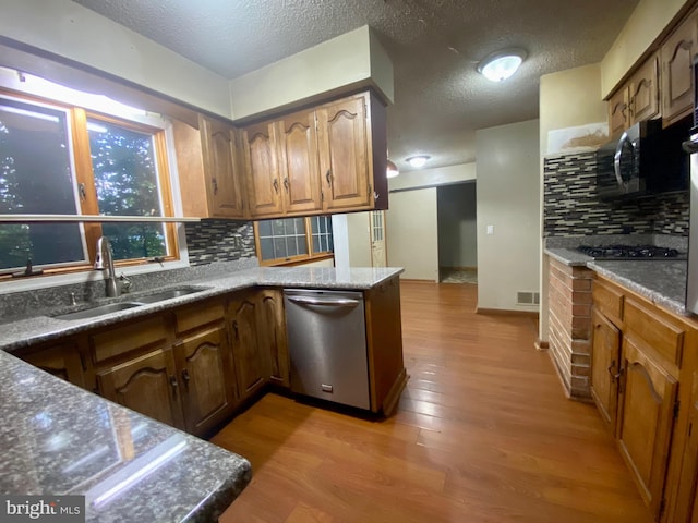 kitchen with a textured ceiling, light hardwood / wood-style floors, sink, backsplash, and appliances with stainless steel finishes