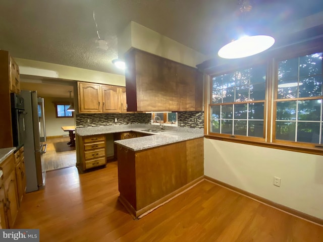 kitchen with sink, light wood-type flooring, kitchen peninsula, and decorative backsplash