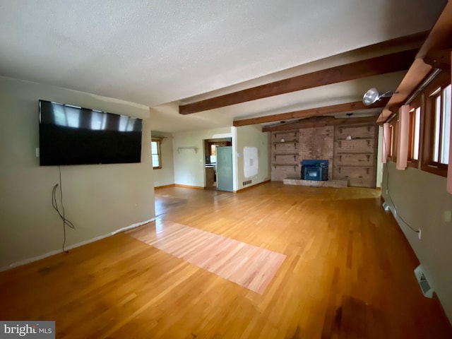 unfurnished living room with a brick fireplace, a textured ceiling, beam ceiling, and wood-type flooring