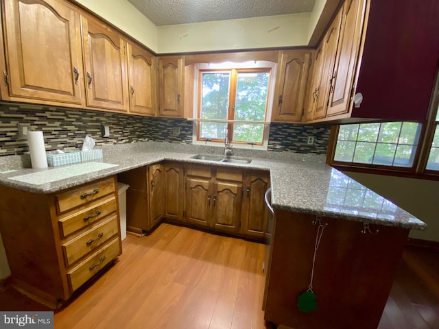 kitchen with backsplash, kitchen peninsula, light wood-type flooring, a textured ceiling, and sink