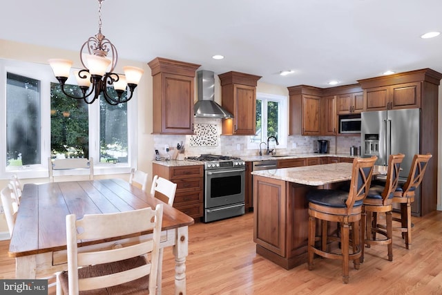 kitchen featuring stainless steel appliances, light hardwood / wood-style flooring, a chandelier, wall chimney exhaust hood, and light stone counters