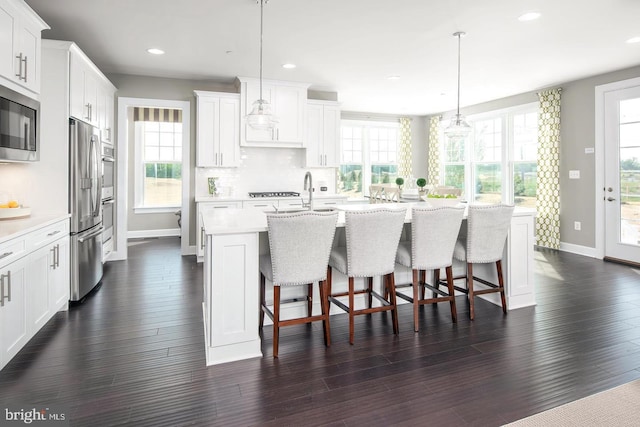 kitchen with dark hardwood / wood-style flooring, stainless steel appliances, a center island with sink, and a wealth of natural light