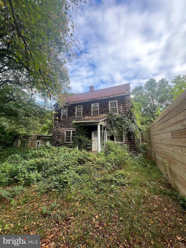 back of property with a chimney, fence, and metal roof