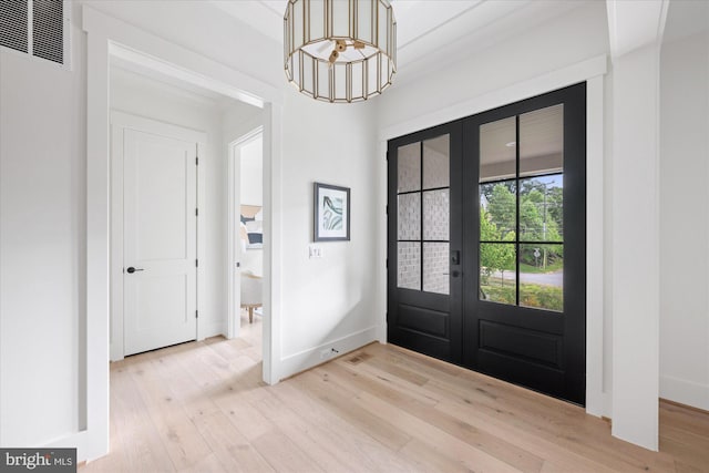 foyer with light wood-type flooring, french doors, and a notable chandelier