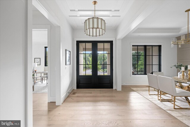 foyer with light wood-type flooring, a tray ceiling, ornamental molding, french doors, and an inviting chandelier