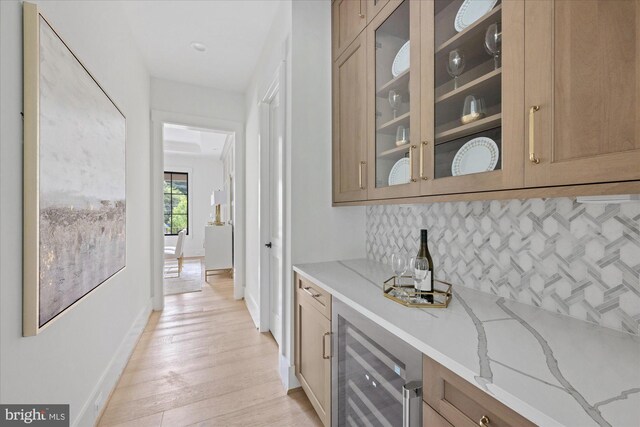 bar featuring backsplash, light stone counters, light hardwood / wood-style floors, and beverage cooler