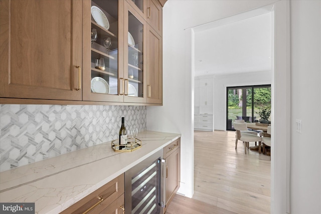 bar with tasteful backsplash, light hardwood / wood-style floors, beverage cooler, and light stone countertops