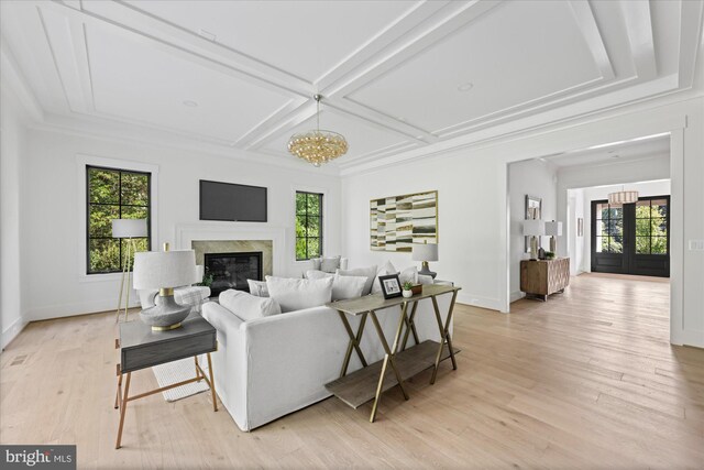 living room featuring coffered ceiling, a notable chandelier, light hardwood / wood-style floors, and a high end fireplace