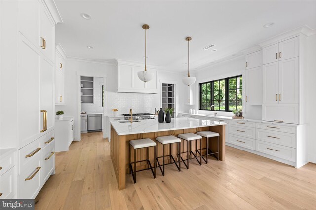 kitchen with light wood-type flooring, a kitchen island with sink, and light stone countertops