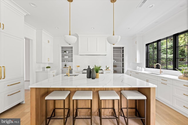 kitchen with sink, decorative light fixtures, light stone counters, and an island with sink