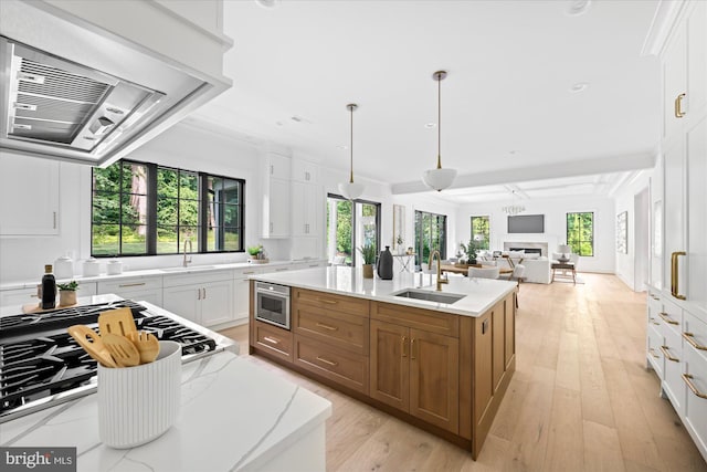 kitchen with sink, plenty of natural light, white cabinets, and an island with sink