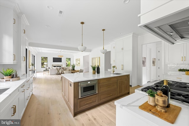 kitchen featuring light wood-type flooring, premium range hood, an island with sink, white cabinets, and light stone counters