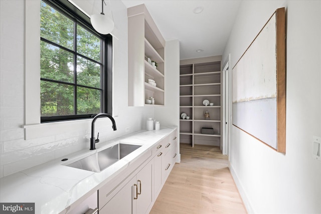 kitchen with sink, light hardwood / wood-style flooring, light stone counters, and a healthy amount of sunlight