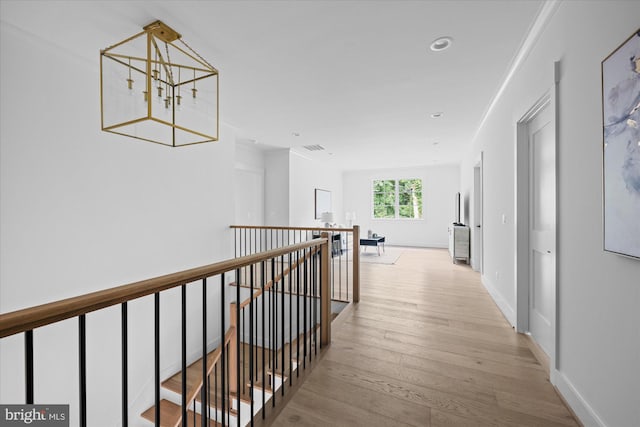 hall featuring light hardwood / wood-style flooring, crown molding, and an inviting chandelier