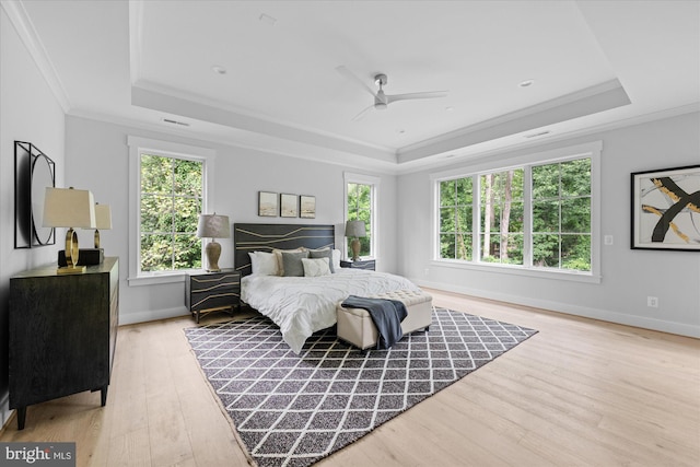 bedroom featuring ceiling fan, a raised ceiling, light hardwood / wood-style flooring, and ornamental molding