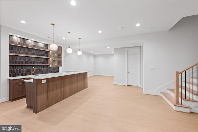 bar featuring sink, decorative light fixtures, dark brown cabinetry, light hardwood / wood-style floors, and tasteful backsplash