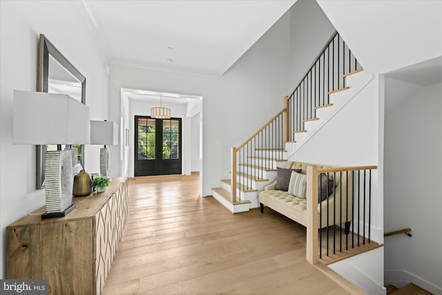 entryway featuring light hardwood / wood-style floors, crown molding, an inviting chandelier, and french doors