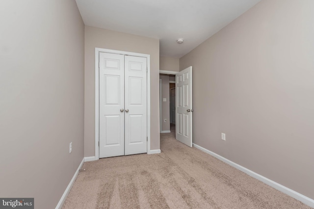 unfurnished bedroom featuring light carpet, baseboards, and a closet