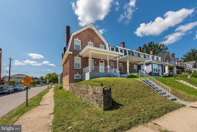 view of front of home with a gambrel roof, a chimney, covered porch, a front lawn, and brick siding