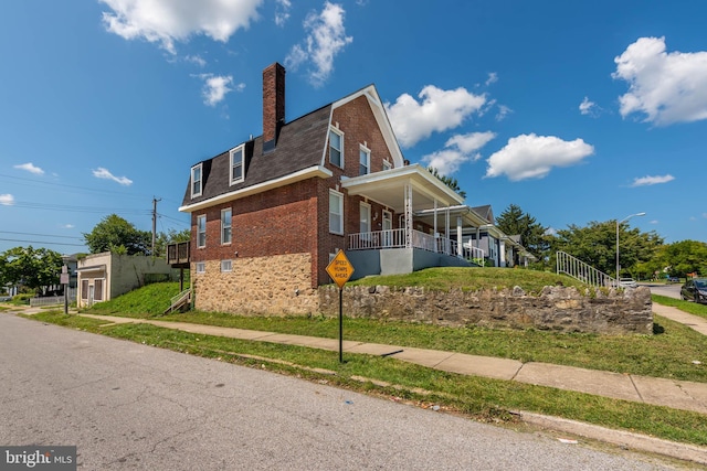 view of home's exterior with brick siding, a chimney, and a gambrel roof