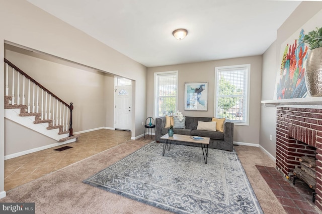 carpeted living area with baseboards, visible vents, tile patterned floors, stairs, and a brick fireplace