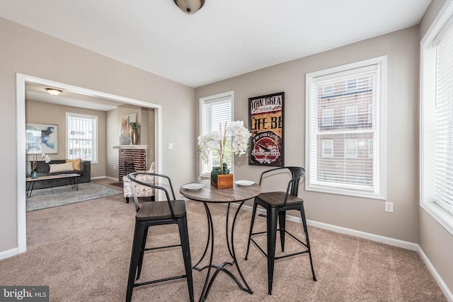 dining space featuring a brick fireplace, light carpet, and baseboards