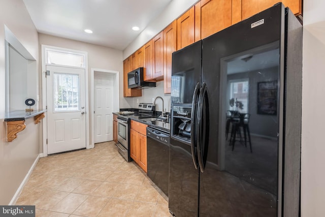 kitchen with light tile patterned floors, a sink, baseboards, black appliances, and brown cabinetry