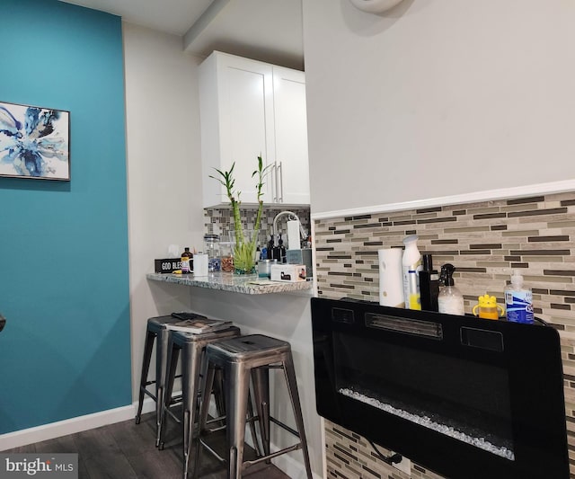 bar with dark hardwood / wood-style floors, light stone countertops, backsplash, and white cabinets