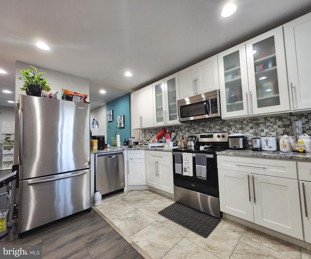 kitchen featuring white cabinets, light stone countertops, stainless steel appliances, and tasteful backsplash